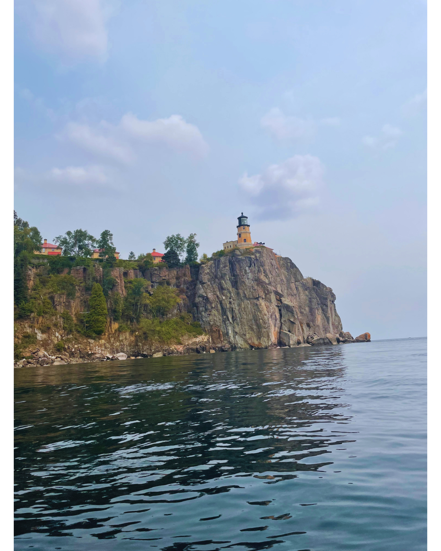 Lighthouse on a rocky cliff overlooking calm water with a clear sky.