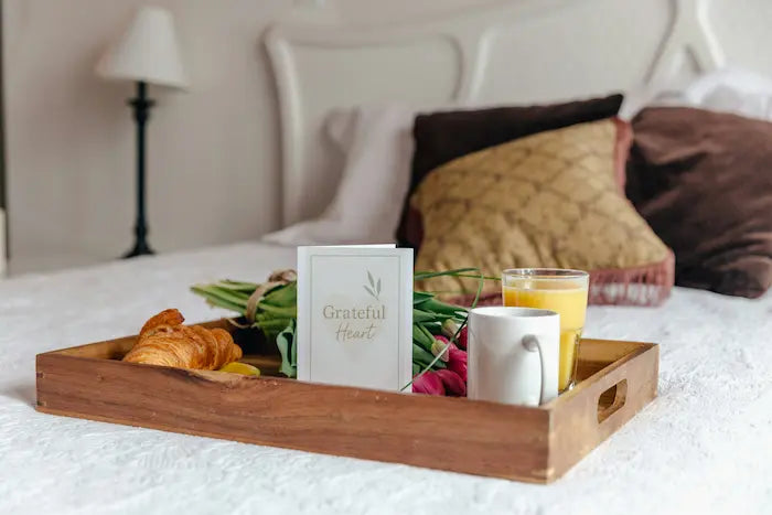Wooden tray with breakfast items on a bed with a Card that says Grateful Heart.