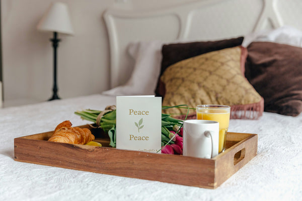 Wooden tray with breakfast items on a bed with a greeting card with the word Peace a leaf and Peace again.